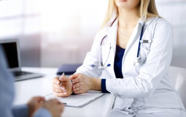 Bilinmeyen kadın doktor, bir klinikteki güneşli dolapta otururken hastasına bazı antibiyotikler yazıyor. Steteskoplu kadın doktor panoya yazı yazıyor.