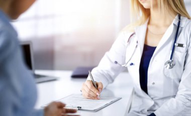Bilinmeyen kadın doktor, bir klinikteki güneşli dolapta otururken hastasına bazı antibiyotikler yazıyor. Steteskoplu kadın doktor panoya yazı yazıyor.