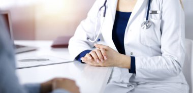 Bilinmeyen kadın-doktor bir klinikteki güneşli dolapta yan yana otururken hastasıyla konuşuyor. Steteskopu olan bir kadın doktor, yakın plan. Mükemmel bir tıbbi hizmet.