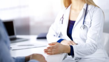 Bilinmeyen kadın-doktor bir klinikteki güneşli dolapta yan yana otururken hastasıyla konuşuyor. Steteskopu olan bir kadın doktor, yakın plan. Mükemmel bir tıbbi hizmet.