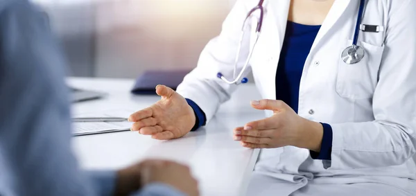 Mujer-médico desconocida está hablando con su paciente, mientras están sentados juntos en el gabinete soleado en una clínica. Médico con estetoscopio en el trabajo, de cerca. Servicio médico perfecto en un — Foto de Stock