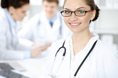 Mutlu gülümseyen kadın doktor tıbbi personelle toplantıda oturup kameraya bakıyor. Tıp konsepti