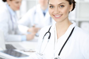 Mutlu gülümseyen kadın doktor tıbbi personelle toplantıda oturup kameraya bakıyor. Tıp konsepti