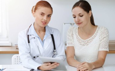 Doktor ve hasta tablet bilgisayar kullanırken oturup sağlık muayenesi sonuçlarını tartışıyorlar. Sağlık, ilaç ve iyi haber kavramları