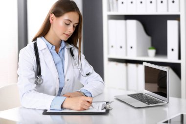 Hastane ofisindeki masada otururken doktor kadın form dolduruyor. Hekim iş başında. İlaç ve sağlık hizmetleri kavramı