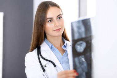 Doktor kadın hastanenin penceresinin yanında dikilirken röntgen filmini inceliyor. Cerrah ya da ortopedist. Tıp ve sağlık hizmetleri kavramı