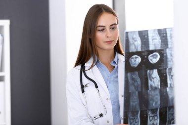 Doktor kadın hastanenin penceresinin yanında dikilirken röntgen filmini inceliyor. Cerrah ya da ortopedist. Tıp ve sağlık hizmetleri kavramı