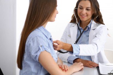 Elinde steteskop olan bir doktor kadın hastasını muayene ediyor. Sağlık, kardiyoloji ve tıp kavramları