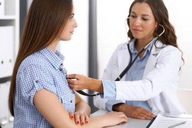 Elinde steteskop olan bir doktor kadın hastasını muayene ediyor. Sağlık, kardiyoloji ve tıp kavramları