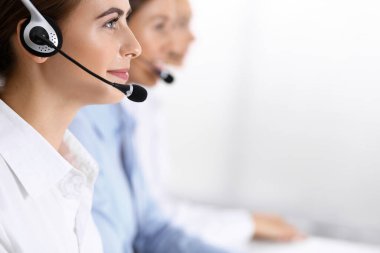 Merkezi ara. Bir grup operatör iş başında. Kulaklıklı güzel iş kadınına odaklan.