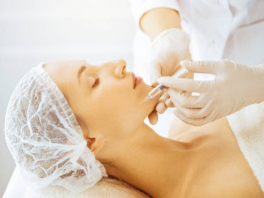 Güzel bir kadın güneşli tıp merkezinde kapalı gözlerle güzellik iğneleri yaptırıyor. Güzellik uzmanı elleri şırıngayla kadın yüzüne güzellik prosedürü uyguluyor.