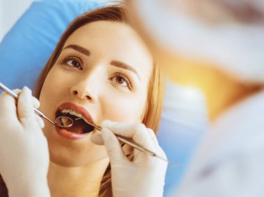 Güneşli diş kliniğinde dişçi tarafından incelenen diş telleriyle gülümseyen genç bir kadın. Sağlıklı diş ve ilaç konsepti