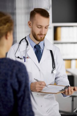 Dost canlısı kızıl sakallı doktor ve hasta kadın güneşli klinikte otururken sağlık muayenesini tartışıyorlar. Tıp konsepti