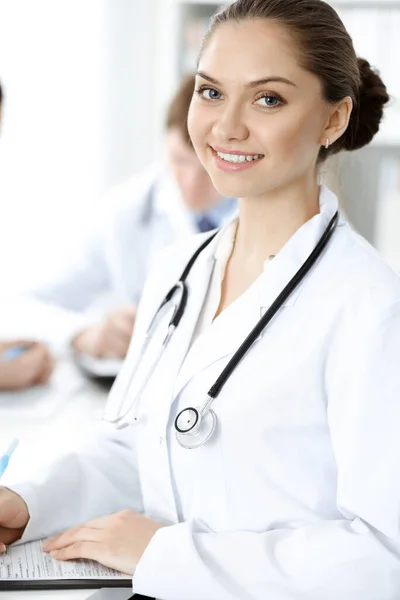 Χαρούμενη χαμογελαστή γυναίκα-γιατρός κάθεται και κοιτάζει την κάμερα σε συνάντηση με το ιατρικό προσωπικό. Έννοια ιατρικής — Φωτογραφία Αρχείου