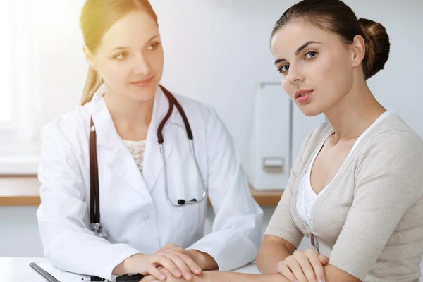 Arzt und Patient sitzen zusammen und besprechen Untersuchungsergebnisse in sonniger Klinik — Stockfoto