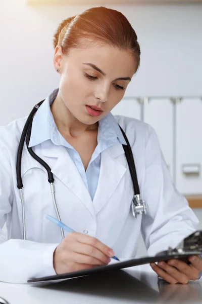 Mulher-médico sentado e trabalhando na clínica ensolarada. Retrato de médica. Conceito de medicina — Fotografia de Stock