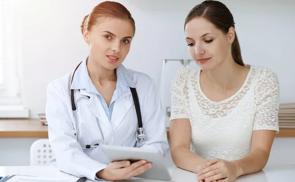 El médico y el paciente están sentados y discutiendo los resultados del examen de salud mientras usan la tableta. Salud, medicina y conceptos de buenas noticias — Foto de Stock