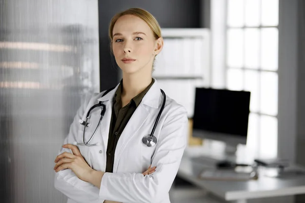 Friendly smiling female doctor standing in clinic. Portrait of friendly physician woman. Perfect medical service in hospital. Medicine concept