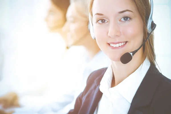 Cheerful smiling business woman with headphones consulting clients. Group of diverse phone operators at work in sunny office.Call center and business people concept Royalty Free Stock Images