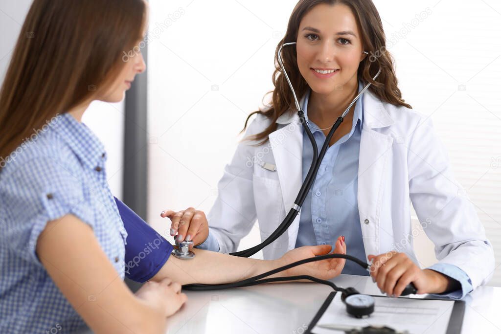 Doctor checking blood pressure of female patient while sitting at the desk in hospital office. Cardiology in medicine and health care concept