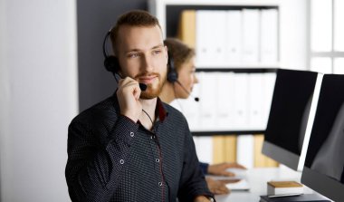 Modern ofiste otururken kulaklıkla konuşan kızıl sakallı bir iş adamı. Çağrı merkezinde çeşitli insanlar var. Tele pazarlama ve müşteri hizmetleri