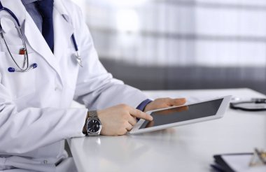 Bilinmeyen erkek doktor klinikteki tablet bilgisayarla yakın planda çalışıyor. İşteki genç doktor. Mükemmel sağlık hizmeti, tıp konsepti