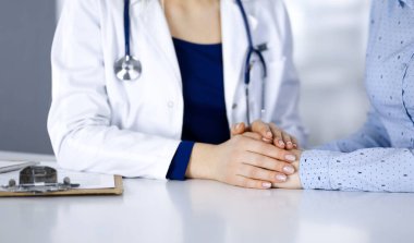 Bilinmeyen kadın doktor, bir klinikteki dolapta yan yana otururken hastasına güven vermek için elini tutuyor. Kadın doktor bir dosya ve steteskop kullanıyor. Kapat.