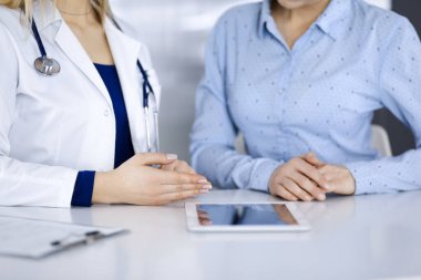 Bilinmeyen kadın-doktor, bir klinikteki dolapta birlikte otururken hastasına bir ilaç tarifi gösteriyor. Kadın hekim bilgisayar tableti ve steteskop kullanıyor.