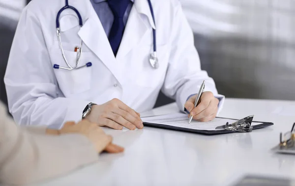 Unknown male doctor and patient woman discussing something while sitting in clinic and using clipboard. Best medical service in hospital, medicine, pandemic stop — Stock Photo, Image