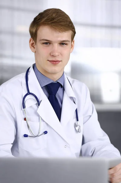 Biondo medico di sesso maschile seduto e che lavora con tablet computer in clinica al suo posto di lavoro, primo piano. Giovane medico al lavoro. Servizio medico perfetto, concetto di medicina — Foto Stock