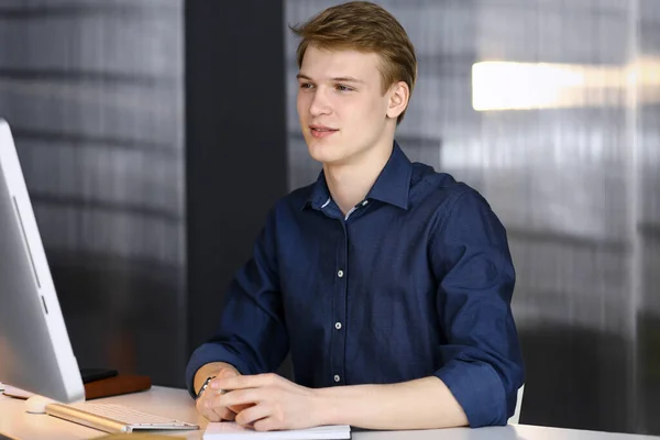 Jeune homme d'affaires blond réfléchissant à la stratégie à son lieu de travail avec ordinateur. Démarrage d'entreprise signifie travailler dur et hors du temps pour la réussite — Photo