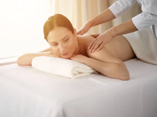Ganska brunett kvinna njuter av proceduren med ryggmassage i solig spa salong. Skönhetsbegreppet — Stockfoto