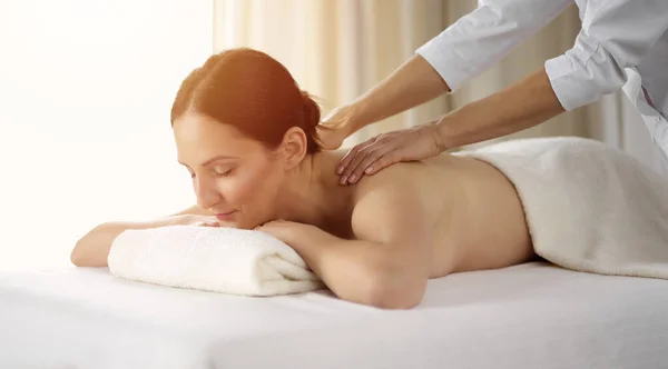 Pretty brunette woman enjoying procedure of back massage in sunny spa salon. Beauty concept Stock Image