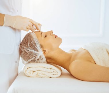 Güneşli tıp merkezinde güzel kadınlara kapalı gözlerle enjeksiyon yapılıyor. Güzellik uzmanı elleri şırıngayla kadın yüzüne güzellik prosedürü uyguluyor.