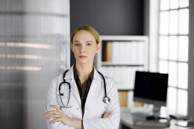 Klinikte duran güler yüzlü bir bayan doktor. Dost canlısı doktor kadın portresi. Hastanede mükemmel bir tıbbi hizmet. Tıp konsepti