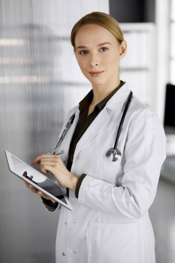 Klinikte tablet bilgisayar kullanan güler yüzlü bir bayan doktor. Hastanede mükemmel bir tıbbi hizmet. Tıp konsepti