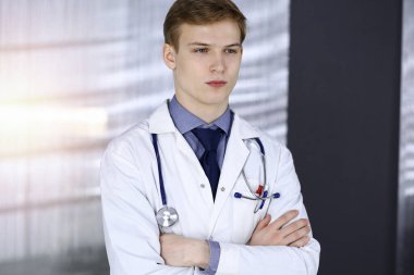 Genç doktor, iş yerinin yakınındaki güneşli klinikte çapraz kollarla duruyor. Tıp konsepti