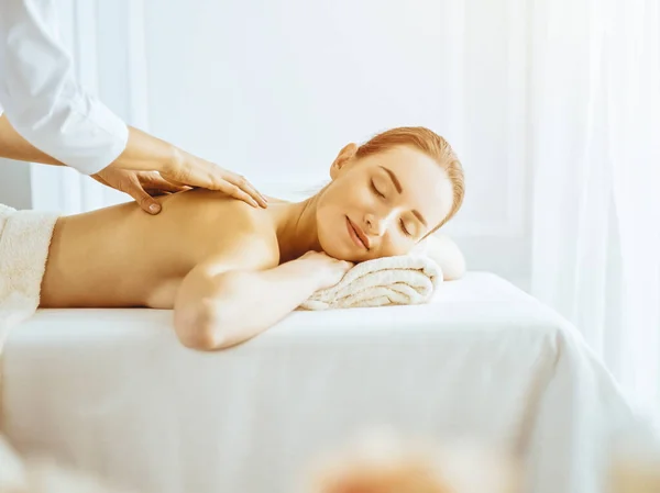 Piękna kobieta korzystających z masażu pleców z zamkniętymi oczami w słonecznym centrum spa — Zdjęcie stockowe