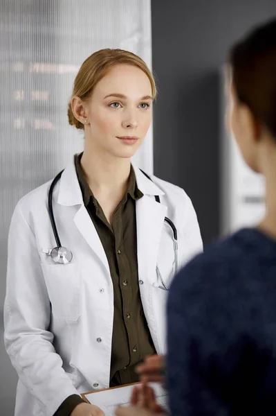 Femme souriante amicale médecin et patiente discutant de l'examen de santé en cours alors qu'elle était assise à la clinique. Médecine et concept de santé — Photo