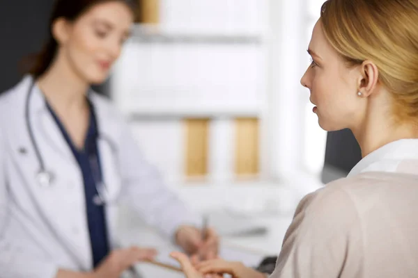 Femme souriante amicale médecin et patiente discutant de l'examen de santé en cours alors qu'elle était assise à la clinique. Médecine et concept de santé — Photo