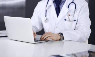 Doktor klinikte dizüstü bilgisayarla oturup çalışıyor, yakın plan. İşteki genç doktor. Mükemmel sağlık hizmeti, tıp konsepti