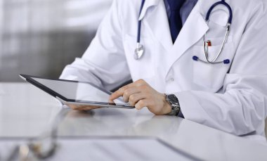 Doktor, klinikteki tablet bilgisayarla yakın plan çalışma odasında oturuyor. İşteki genç doktor. Mükemmel sağlık hizmeti, tıp konsepti