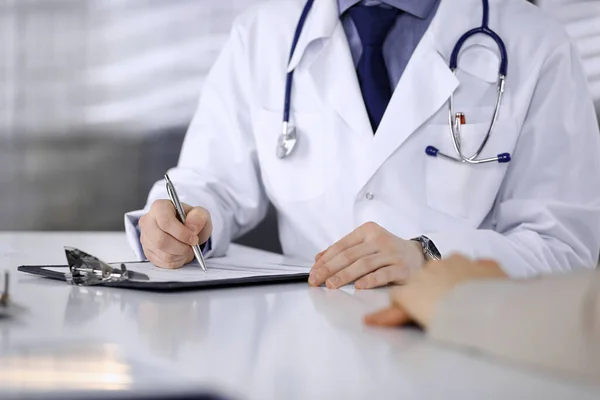 Unknown male doctor and patient woman discussing something while sitting in clinic and using clipboard. Best medical service in hospital, medicine, pandemic stop — Stock Photo, Image