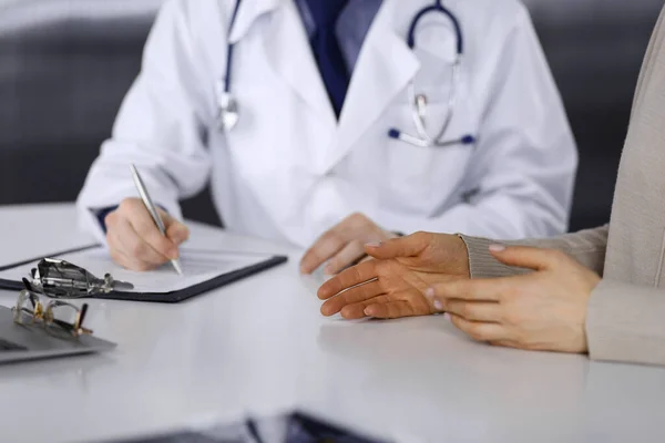 Doctor and patient woman discussing something while sitting in clinic and using clipboard. Best medical service in hospital, medicine, pandemic stop — Stock Photo, Image