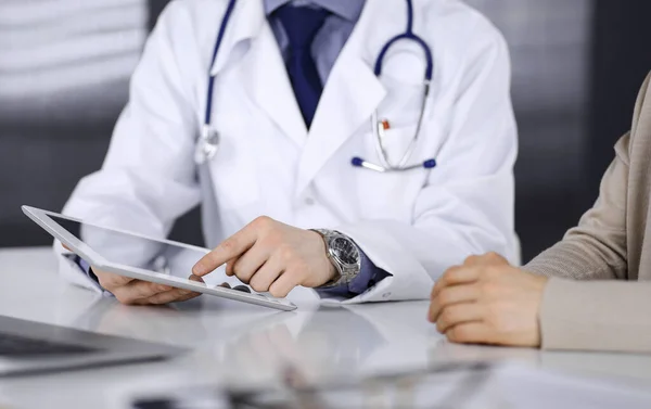 Desconocido médico masculino y mujer paciente discutiendo algo mientras está sentado en la clínica y el uso de la tableta. El mejor servicio médico en hospital, medicina, parada pandémica — Foto de Stock