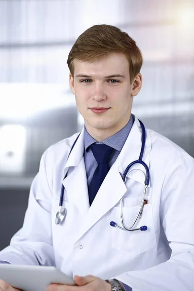 금발 남성 의사 가 직장에서 태블릿 컴퓨터와 함께 앉아서 일하고 있습니다. 의학적 개념 — 스톡 사진