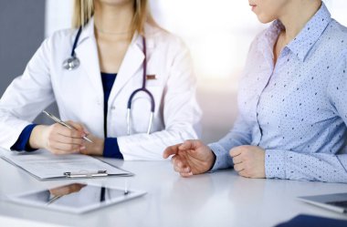 Bilinmeyen kadın. Doktor, bir klinikteki güneşli dolapta birlikte otururken hastasını dinliyor. Steteskoplu kadın doktor panoya yazı yazıyor, kapat. Mükemmel.