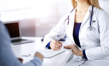 Bilinmeyen kadın doktor, bir klinikteki güneşli dolapta otururken hastasına bazı antibiyotikler yazıyor. Steteskoplu kadın doktor panoya yazı yazıyor.