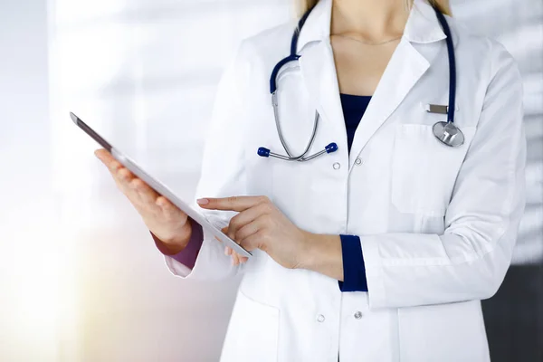 Neznámá žena-doktorka drží v rukou tablet, zatímco stojí ve slunné skříňce na klinice. Ženský lékař v práci, zblízka. Perfektní lékařská služba v nemocnici. Koncept medicíny — Stock fotografie