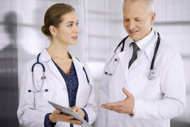 Yaşlı, kendine güvenen doktor ve kadın doktor klinikte dururken güncel hastalık terapisini tartışıyorlar. Hastanede takım çalışması. Tıp ve sağlık hizmetleri kavramı